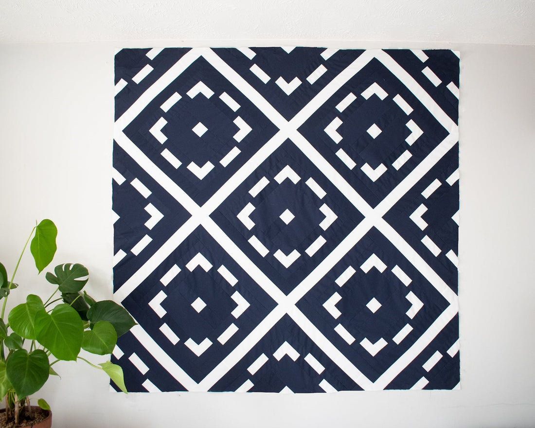 A modern quilt design that shows white circular shapes in a lattice outline on a dark navy background and a green plant in the left hand corner adorns the image